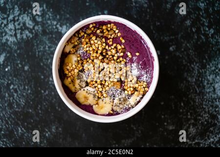 Take away Vegan Food Acai Bowl con latte di mandorle, burro di arachidi, banana, grano saraceno granola, Cia Seeds e pezzi di cioccolato in cartone Bowl. Org sano Foto Stock