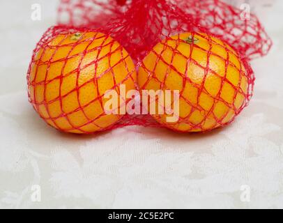 Due satsuma in borsa rossa in rete di nylon che si trovano sulla tovaglia damask Foto Stock