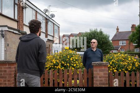 David Blohm (a destra) parla con il suo vicino Jack Gutteridge attraverso il confine di blocco dalla sua casa su Telford Way a Leicester. David Blohm e Jack Gutteridge vivono accanto l'uno all'altro, ma si trovano sui lati opposti del confine dopo che un blocco locale è stato imposto a seguito di un picco nei casi di coronavirus nella città. Foto Stock