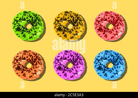 Ciambelle colorate su sfondo giallo. Concetto di estate minimo. Layout piatto, vista dall'alto. Foto Stock