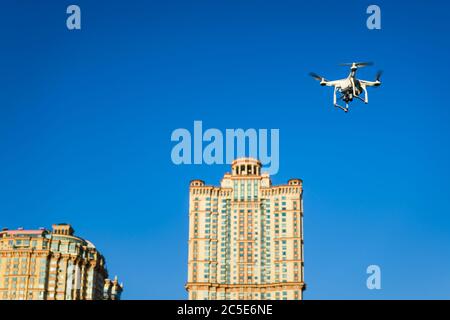 Drone quad copter con fotocamera digitale ad alta risoluzione a bordo che vola sullo sfondo della città nel cielo blu Foto Stock