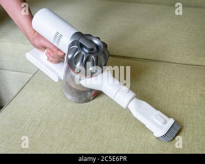 Aspirapolvere wireless utilizzato sul divano in camera. Lavori domestici con nuovo gancio verticale e bocchetta. La persona può utilizzare un aspirapolvere bianco moderno. Pulizia della casa, c Foto Stock
