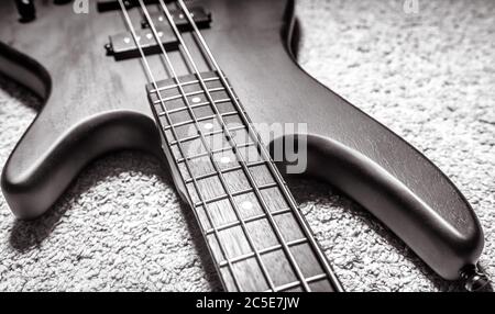 Chitarra basso con quattro corde in primo piano bianco e nero. Dettaglio del popolare strumento musicale rock. Vista ravvicinata dei bassi elettrici sul tappeto. Vintage st Foto Stock