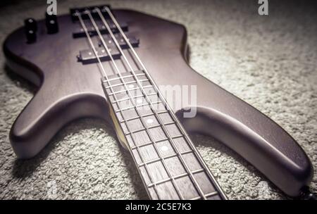 Chitarra basso con quattro corde closeup. Dettaglio del popolare strumento musicale rock. Vista ravvicinata dei bassi elettrici marroni sul tappeto, messa a fuoco selettiva. Vintag Foto Stock