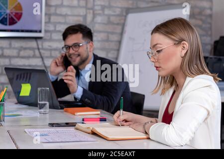 Business manager che parla sul telefono cellulare e una bella giovane segretaria o donna d'affari, lavorando insieme in un moderno ufficio in stile retrò. Avvio. Foto Stock
