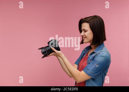 Ritratto di giovane fotografa femminile isolato su sfondo rosa con spazio per la copia. Fotografo con fotocamera professionale che scatta foto in studio fotografico Foto Stock