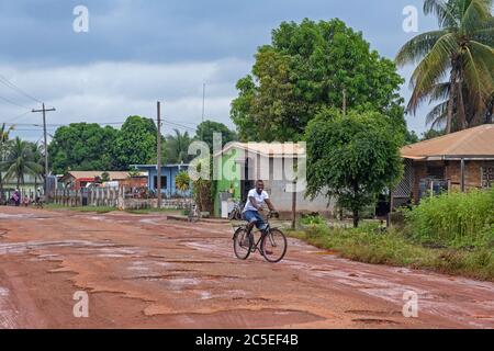 Ciclista locale che corre lungo la strada fangosa sterrata nel villaggio di Lethem durante la stagione delle piogge, alta Takutu-Upper Essequibo regione, Guyana, Sud America Foto Stock