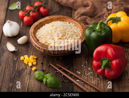 Ciotola con riso vegetale basmati a grani lunghi bollito su fondo di legno con bastoncini e pepe di paprika con mais, aglio, basilico e pomodori. Foto Stock