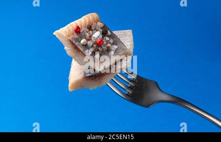 Pezzi di aringa salata su forchetta isolati su sfondo blu Foto Stock