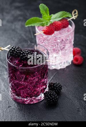 Cocktail estivo con mora e limonata rosa in bicchieri di cristallo con cubetti di ghiaccio e menta su sfondo nero. Miscela di bevande analcoliche e alcol. Macro