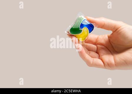 La capsula per lavastoviglie può essere tenuta a mano su sfondo beige. Spazio per la copia. Donna che tiene la compressa detergente per lavastoviglie a mano. Foto Stock