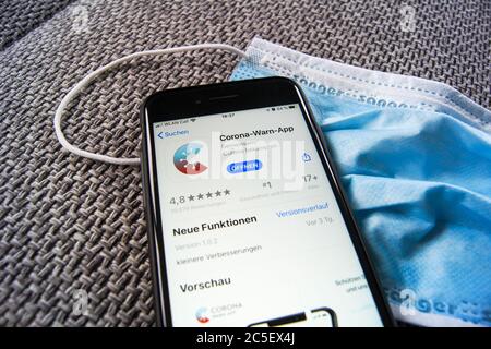 Corona WARN App del governo federale tedesco nell'Apple App Store su uno smartphone che si trova su una maschera protettiva. Foto Stock