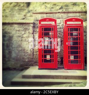 Un paio di tradizionali scatole telefoniche rosse inglesi contro il muro del Castello di Edimburgo, Scozia. Elaborazione incrociata per avere un aspetto simile a quello di una foto istantanea obsolete. Foto Stock