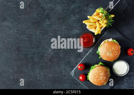 Menu fast food con hamburger, patatine fritte e salsa di ketchup su sfondo nero vista dall'alto. Spazio di copia. Foto Stock