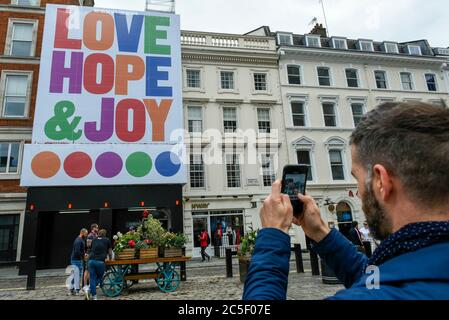 Londra, Regno Unito. 2 luglio 2020. Un passer con fotografie un poster che mostra il testo 'Amore, speranza e gioia' che si affaccia sulla Piazza in Covent Garden. L'opera d'arte di Anthony Burrill è la sua più grande fino ad oggi e celebra la riapertura della zona a acquirenti e aziende dopo che alcune limitazioni di blocco pandemiche del coronavirus sono state rilassate. I lavori saranno in mostra fino al 2020 ottobre. Credit: Stephen Chung / Alamy Live News Foto Stock