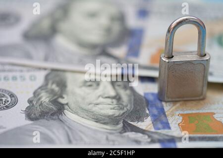 Lucchetto in metallo su fondo di banconote da 100 dollari USA. Stack di denaro per la sicurezza e gli investimenti. Concetto di risparmio e sicurezza finanziaria Foto Stock