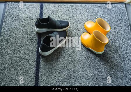 Primo piano vista delle scarpe estive gialle e nere sul tappetino vicino alla porta d'ingresso. Concetto di scarpe per bambini. Foto Stock