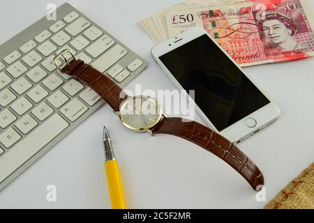 Nota inglese di cinquanta libbre con tastiera bianca e orologio da polso e cellulare su sfondo bianco, concetto finanziario Foto Stock