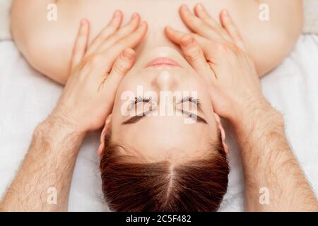 Le mani del terapeuta di massaggio stanno mettendo le pietre di massaggio sugli occhi della donna giovane durante il massaggio dell'occhio. Foto Stock