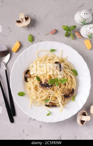 Spaghetti con funghi e basilico su piatto bianco su fondo grigio, primo piano Foto Stock