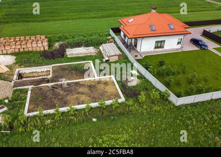 Veduta aerea di una casa privata con finestre soffitta sul tetto, cortile pavimentato con prato verde erba e cantiere con pavimento in cemento e s. Foto Stock