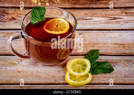 Tazza di tè nero preparato con menta e limone su tavolo di legno. Foto Stock