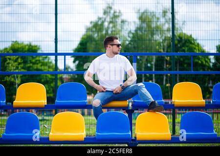 Un ragazzo in una T-shirt bianca si siede in uno stadio sulle sedie per i fan da soli. Foto Stock