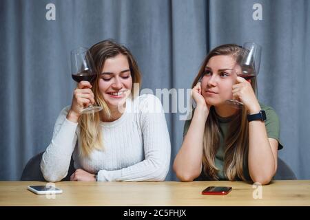 Due ragazze di aspetto europeo con capelli biondi sono seduti al tavolo, bere vino e ridere, rilassarsi a casa, alcol Foto Stock