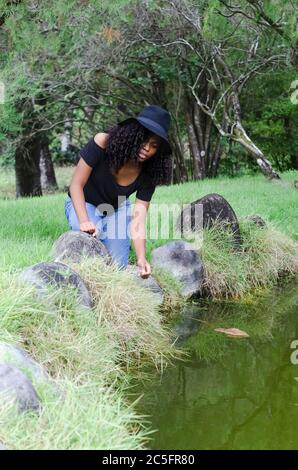 una giovane donna nera tra i 20 e i 30 anni seduta a leggere un libro da sola, in un parco, circondato da alberi Foto Stock