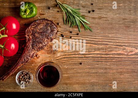 Barbecue costolette di manzo stagionato con verdure e bicchiere di vino rosso da vicino su sfondo di legno Foto Stock