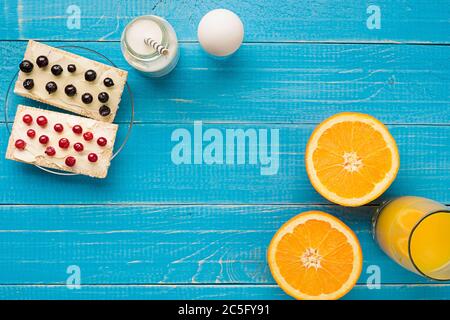 Colazione sana. Panini dolci con formaggio spalmabile e frutti di bosco freschi e frutta su sfondo blu. Foto Stock