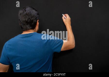 Classe di un insegnante con la schiena scritta su una lavagna con un gesso Foto Stock