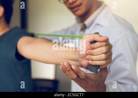 La discesa del terapeuta fisico maschile asiatico lavora e contribuisce a proteggere le mani dei pazienti con il paziente che fa esercizio di stretching con un exer flessibile Foto Stock