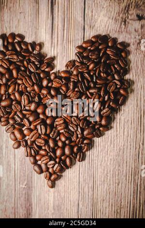 una manciata di chicchi di caffè a forma di cuore, primo piano. chicchi di caffè a forma di cuore arrostiti sul tavolo, fuoco selettivo. Tema romantico. Foto Stock
