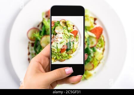 Fotografia del concetto di cibo - donna scatta foto di insalata fresca con lattuga, ravanelli, pompelmo, formaggio e condimento di agrumi Foto Stock