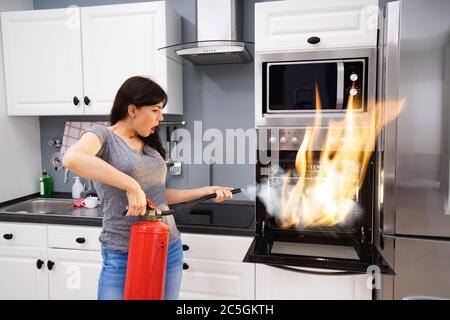 Giovane donna con un estintore per spegnere un incendio dal forno a casa Foto Stock