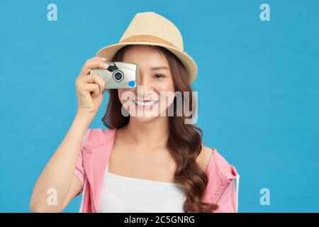 Attraente donna asiatica energica felicemente tenendo cemara isolato su sfondo blu studio Foto Stock