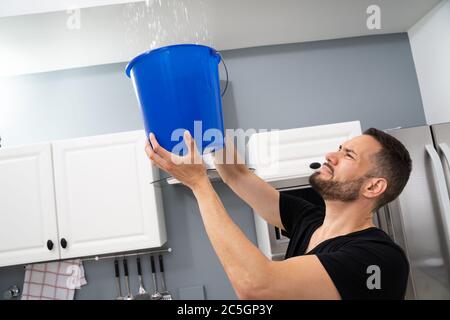 Benna di tenuta dell'uomo preoccupata mentre goccioline di acqua fuoriescono dal soffitto in cucina Foto Stock