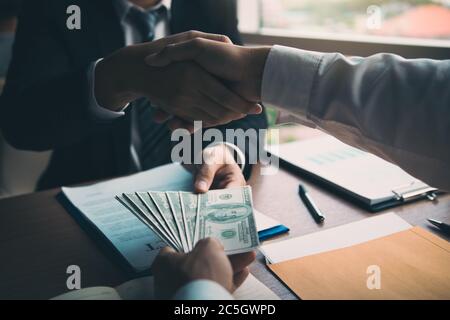 Due uomini d'affari aziendali scuotono le mani mentre un uomo dà denaro e riceve denaro sporco in ufficio con concetto di corruzione. Foto Stock