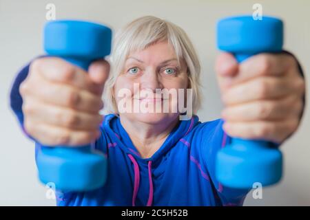 Donna anziana in blu facendo le sue esercitazioni con i manubri. Ritratto di donna anziana sorridente con manubri. Primo piano di donna anziana sollevamento manubri Foto Stock