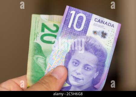 Le persone mano dando la valuta del Canada - un viola dieci dollari e venti note verdi con Viola Desmond si sparse su uno sfondo marrone. LUN Foto Stock