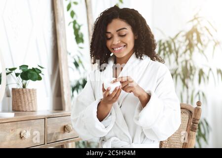 Crema per la cura della pelle. Sorrido Afro American Woman Holding vaso con idratante lozione Foto Stock