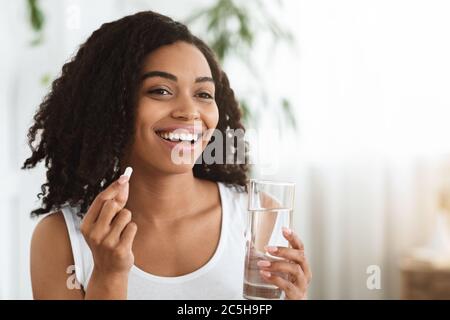 Alimentazione sana. Sorridente Afro Donna che tiene la pillola di vitamina e acqua minerale Foto Stock