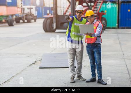 Il team di lavoro per la logistica si combina con il controllo online wireless dei laptop che carica i container al porto di carico ai camion per l'esportazione e l'importazione Foto Stock