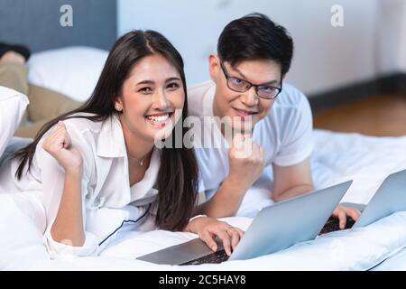 Squadra di coppia asiatica che lavora a casa sul letto con il laptop buon divertimento con la fotocamera ritratto di successo. Foto Stock