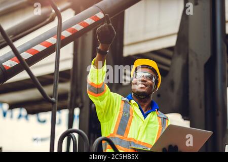 Lavoratore nero afroamericano come caposquadra orgoglioso di felice sorriso di lavoro controllo carico carico carico in magazzino logistica di spedizione con tuta di sicurezza. Foto Stock