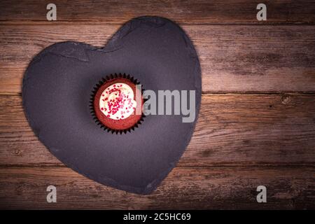 San Valentino regalo di una cupcake di velluto rosso su un cuore di ardesia, su sfondo di legno vecchio., con spazio per il testo Foto Stock