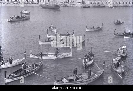 Anni '20, immagine storica che mostra numerose gondole veneziane e traghetti sul Canal Grande o laguna a Venezia, Italia, incantando i passeggeri, con il loro equipaggio o i loro aristi, noti come gondolieri. I Traghetti sono simili alle gondole affittate privatamente, appositamente progettate per l'uso sui corsi d'acqua veneziani, ma sono traghetti pubblici in gondola. Foto Stock