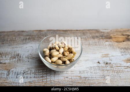 Pistacchi in un piccolo piatto su un tavolo di legno d'epoca. Il pistacchio è un alimento nutriente sano vegetariano della proteina. Spuntini naturali alla frutta secca. Foto Stock