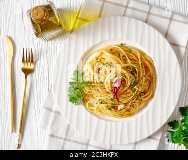 Spaghetti alla colatura di alici, spaghetti con salsa di acciughe, pepe pimento, aglio e prezzemolo su un piatto bianco su un tavolo di legno bianco, orizzontale Foto Stock